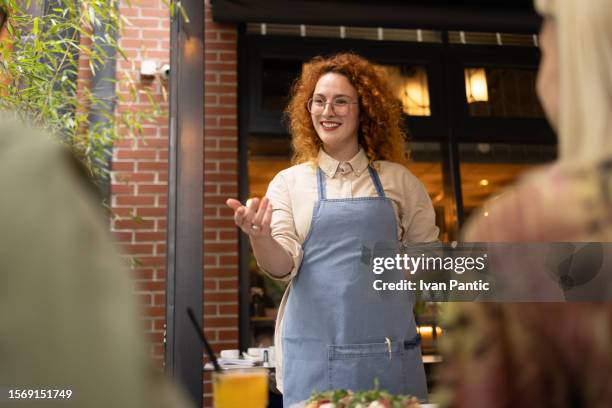 camarera pelirroja feliz tomando pedidos de clientes en un café. - camarera fotografías e imágenes de stock