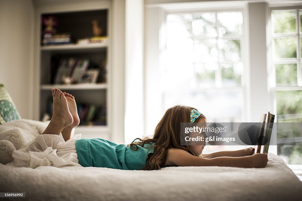 Girl (6yrs) reading book on bed