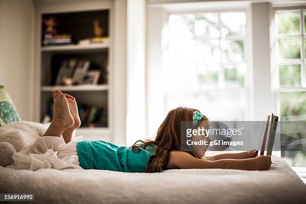 girl (6yrs) reading book on bed - child reading a book stockfoto's en -beelden