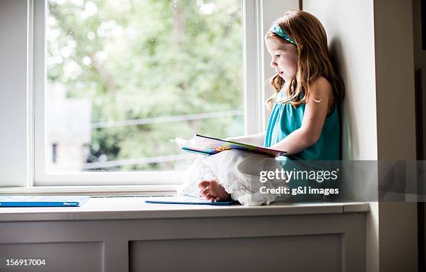 girl (6yrs) sitting in window reading a book - window sill stock pictures, royalty-free photos & images