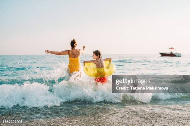 young mother with little son runs into the sea on sunset light. rear view. - swimwear stock pictures, royalty-free photos & images