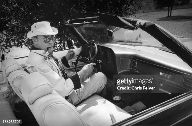 Portrait of American journalist and author Hunter S Thompson as he sits behind the wheel of a Pontiac Grand Ville convertible, 1990. He has a...