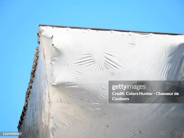 a white plastic tarpaulin hides the scaffolding erected in front of a building under construction in paris, france - plane in sky stock-fotos und bilder