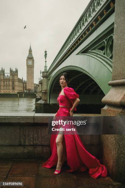 stylish fashion model posing in pink dress at iconic westminster bridge with big ben and parliament building in background on a windy, rainy day - day uk show stockfoto's en -beelden