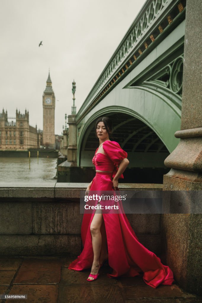 Stylish Fashion Model Posing in Pink Dress at Iconic Westminster Bridge with Big Ben and Parliament Building in Background on a Windy, Rainy Day