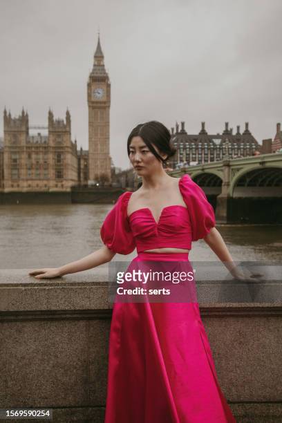 stylish fashion model posing in pink dress at iconic westminster bridge with big ben and parliament building in background - woman fashion model stock pictures, royalty-free photos & images