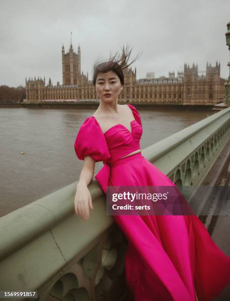 graceful fashion model embracing the elements at westminster bridge with big ben, elizabeth tower, and parliament building on a windy, rainy day - collection launch street style stock pictures, royalty-free photos & images
