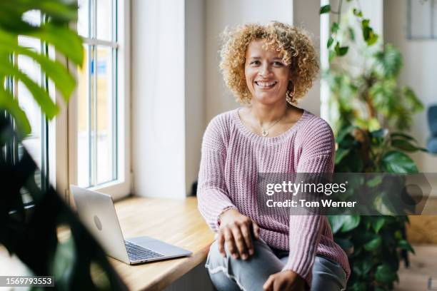 portrait of woman with curly hair using laptop by window - einzelne frau über 40 stock-fotos und bilder
