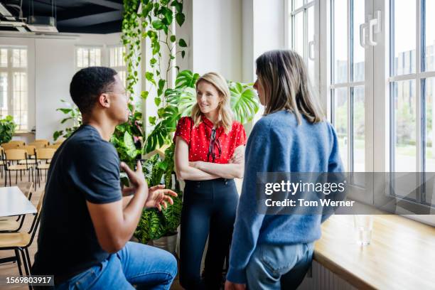 three work colleagues talking while standing by window - better hearing stock pictures, royalty-free photos & images