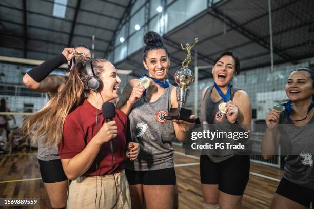 junge tv-reporterin interviewt weibliche volleyballmannschaft nach dem sieg eines spiels auf dem sportplatz - reportage award winners stock-fotos und bilder