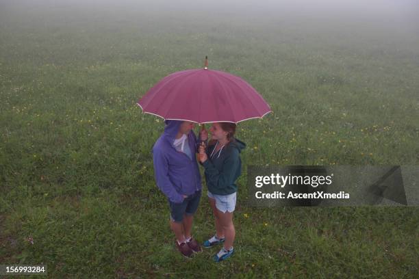 teenage kids huddling under an umbrella - sharing umbrella stock pictures, royalty-free photos & images