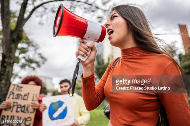 teenage girl shouting on megaphone on an environmental protest outdoors - march stock pictures, royalty-free photos & images