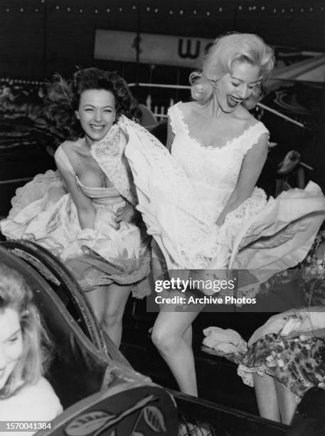 Two women laughing as they hold the skirts of their dresses down while standing on the wind machine at the Festival Gardens Fun Fair, held at...