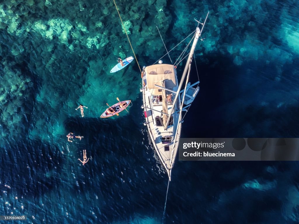 High angle view of distant people swimming by modern sailboat on sea