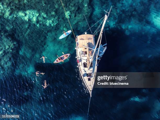 high angle view of distant people swimming by modern sailboat on sea - sailing greece stock pictures, royalty-free photos & images