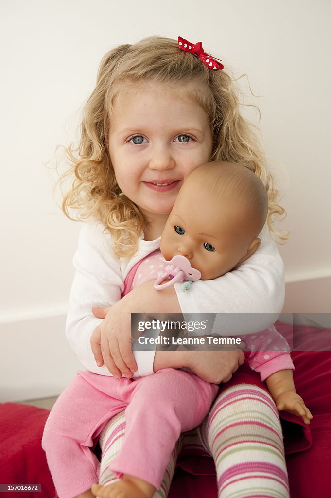 Two year old blonde girl nursing a baby doll