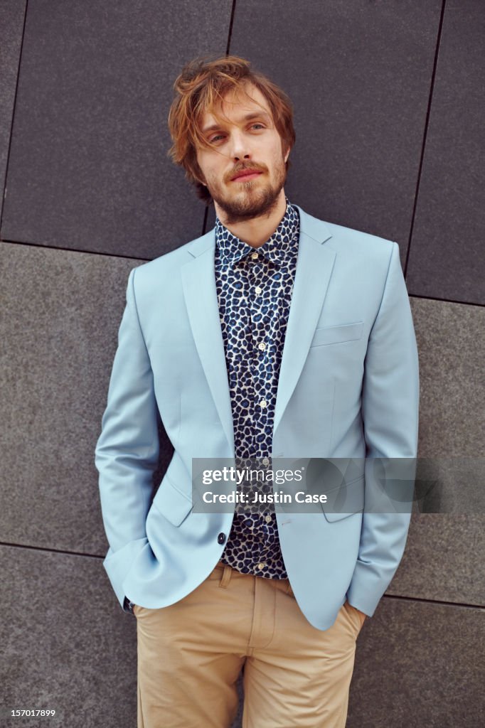 A trendy man leaning against a stone wall