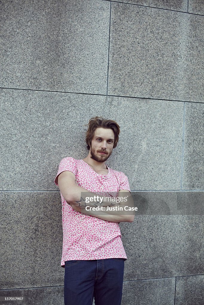 A handsome man leaning against a stone wall