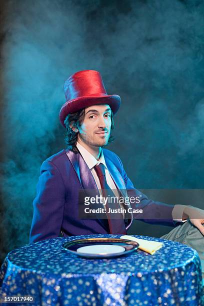 a magician sitting in front  of table - sombrero púrpura fotografías e imágenes de stock