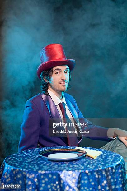 a magician sitting in front  of table - chapeau haut de forme photos et images de collection