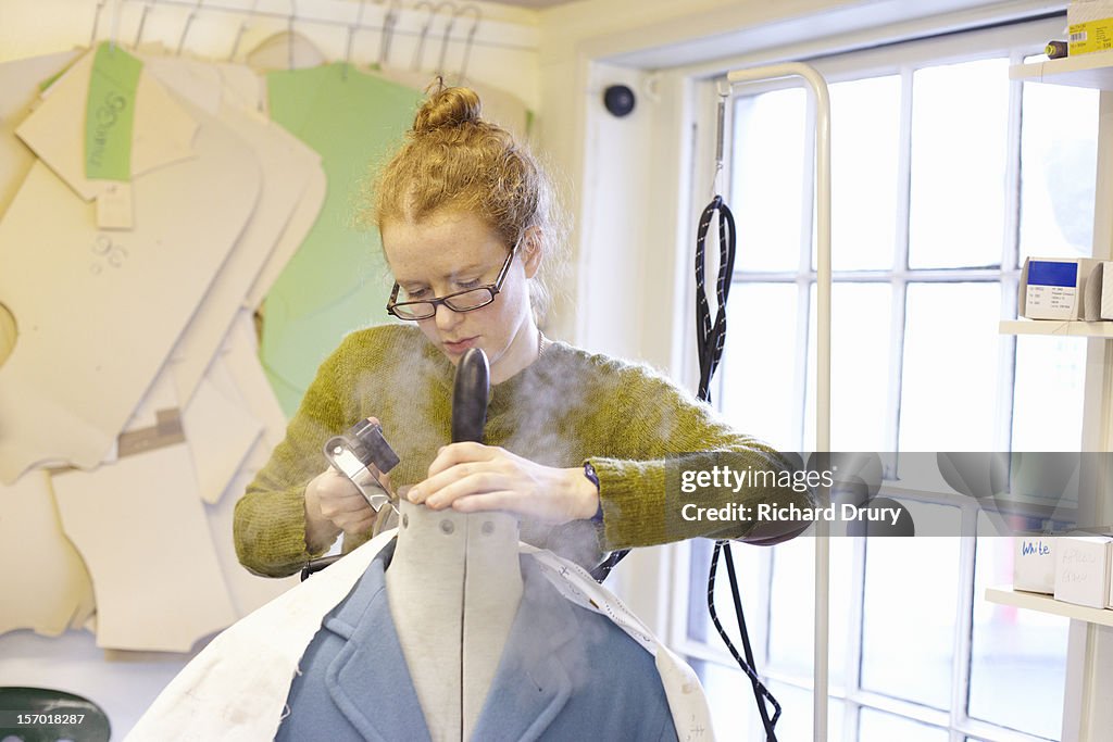 Woman using steam iron in clothing workshop