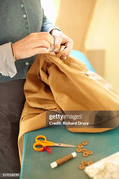 woman sewing button on garment - button craft stock pictures, royalty-free photos & images