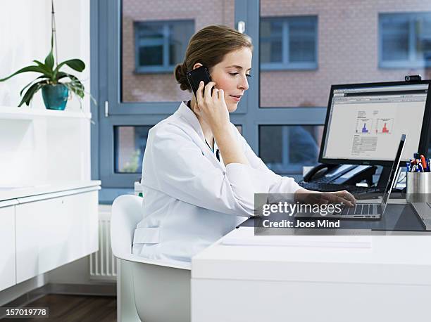 female doctor on smart phone, using laptop - arzt praxis stock-fotos und bilder