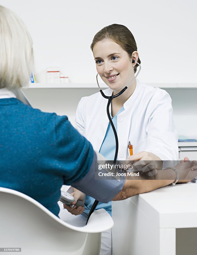 Doctor checking patients blood pressure, smiling