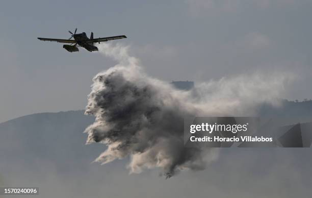 An AT-802F Fire Boss firefighting amphibious aircraft flies over heavy smoke to drop water at a forest fire being fought by 409 operatives are...