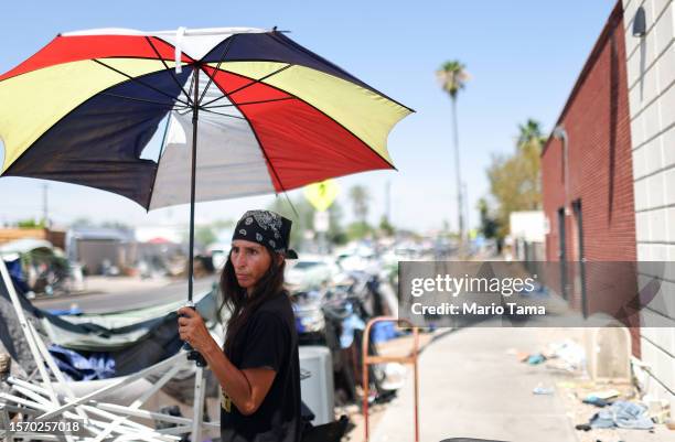 Roni stands beneath an umbrella in a section of the 'The Zone', Phoenix's largest homeless encampment, amid the city's worst heat wave on record on...