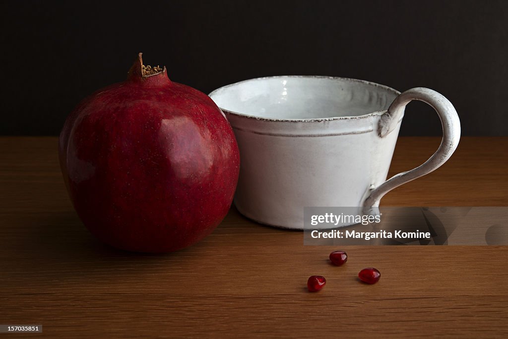 Pomegranate fruit, white cup and three arils