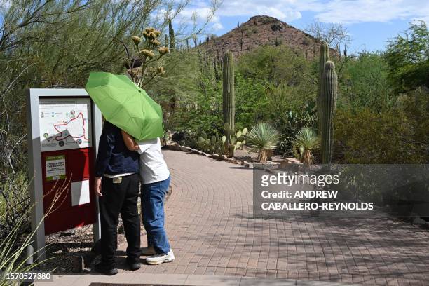 Two people look at a map as they use an umbrella, shield themselves from the sun as they walk through the Phoenix botanical gardens in Phoenix...