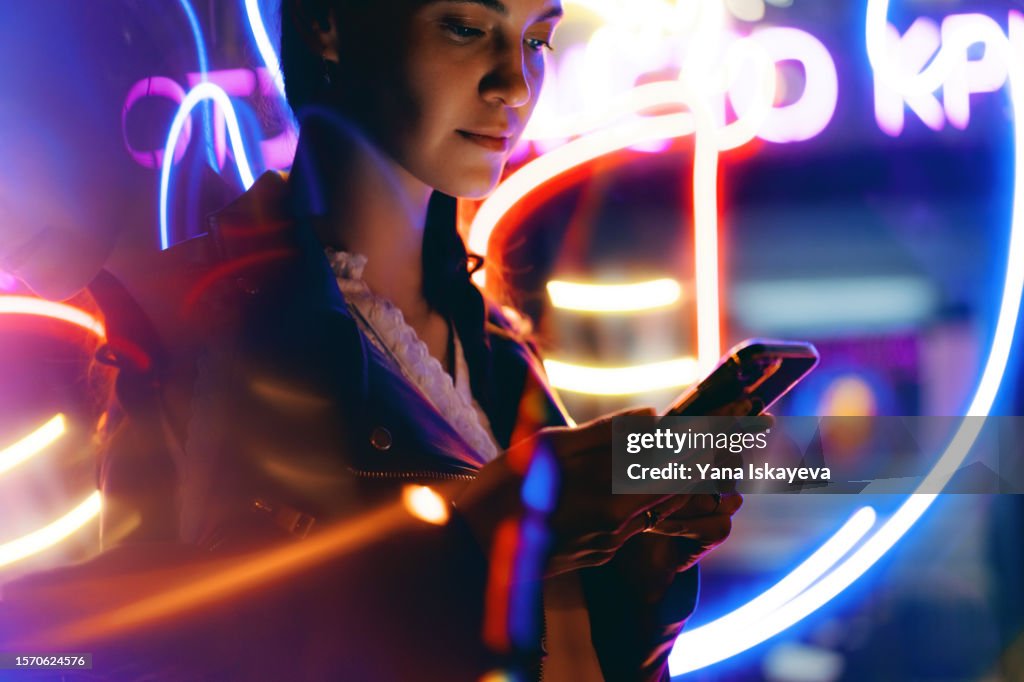 Progressive woman is using mobile phone at night in neon lights