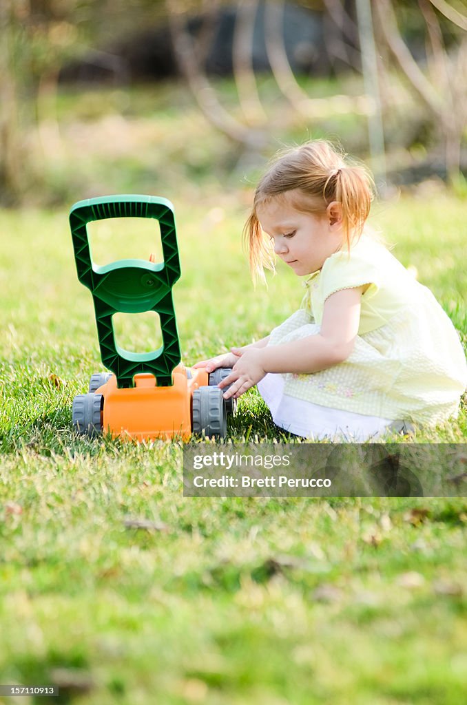 Toddler girl fixing her toy lawn mower