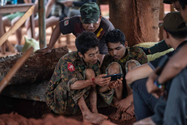 Two regime soldiers who were captured by Karenni resistance forces watch video footage with a mobile phone in an undisclosed area in Kayah state. Two...
