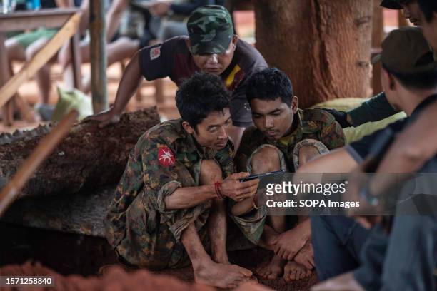 Two regime soldiers who were captured by Karenni resistance forces watch video footage with a mobile phone in an undisclosed area in Kayah state. Two...