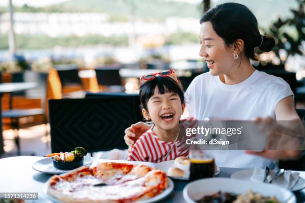 young asian mother taking selfies with lovely little daughter with smartphone in an outdoor restaurant joyfully. happy young asian family enjoying time together while dining out - chinese family taking photo at home stock pictures, royalty-free photos & images