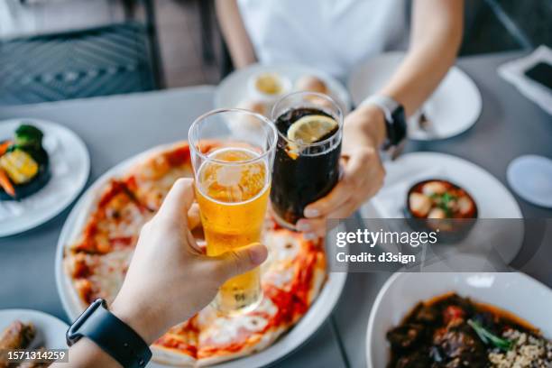 cropped shot of a couple having a good time together and making a toast while enjoying delicious lunch in an outdoor restaurant, with pizza and assorted dishes sharing on the dining table - soda photos et images de collection