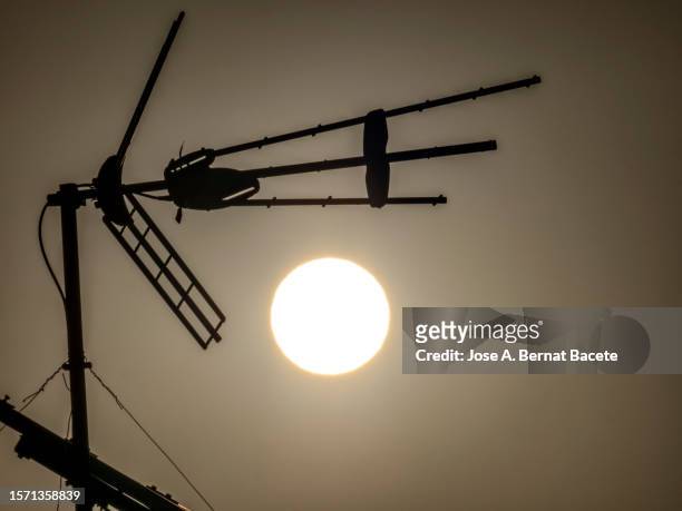 clear sky with the sun and the silhouette of an antenna on the roof on a very hot day. - television aerial stock pictures, royalty-free photos & images