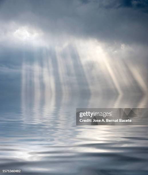 clouds in the sky with sunbeams reflected on a water surface. - cirrus stockfoto's en -beelden