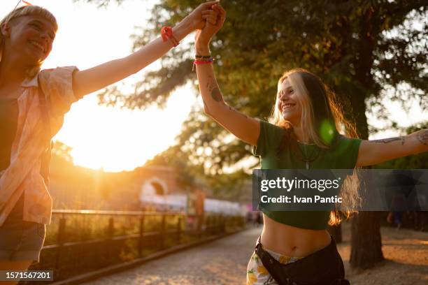 carefree women holding hands during a music festival at sunset. - park festival stock pictures, royalty-free photos & images