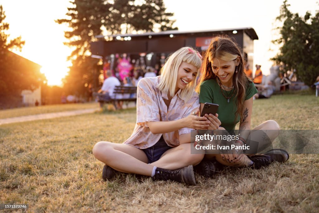 Des festivalières heureuses utilisant un téléphone intelligent au coucher du soleil.