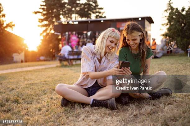 happy female festival goers using smart phone at sunset. - amizade imagens e fotografias de stock