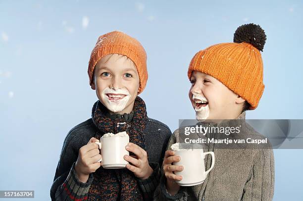 two kids having fun in the snow drinking hot chocolate - traditionele koksmuts stockfoto's en -beelden