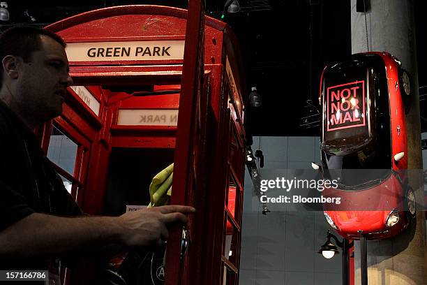 An employee cleans a phone booth standing beneath a Mini Cooper automobile, by Bayerische Motoren Werke AG , hanging from a pillar during the LA Auto...