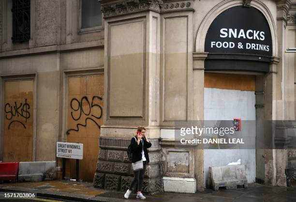 Pedestrian speaks on a phone as they walk past a boarded-up a closed-down store near Piccadilly Circus, in central London on August 2, 2023....