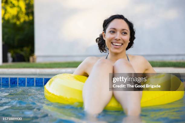 young woman floating on raft in swimming pool - schwimmbeckenrand stock-fotos und bilder