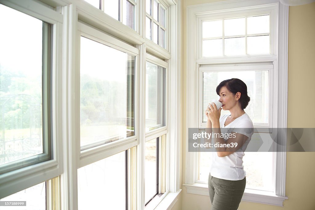 Woman standing by a window drinking coffee
