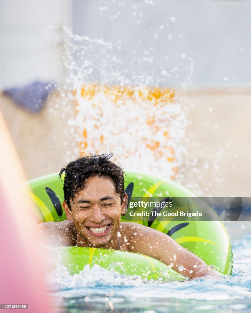Young man floating on pool raft and splashing water