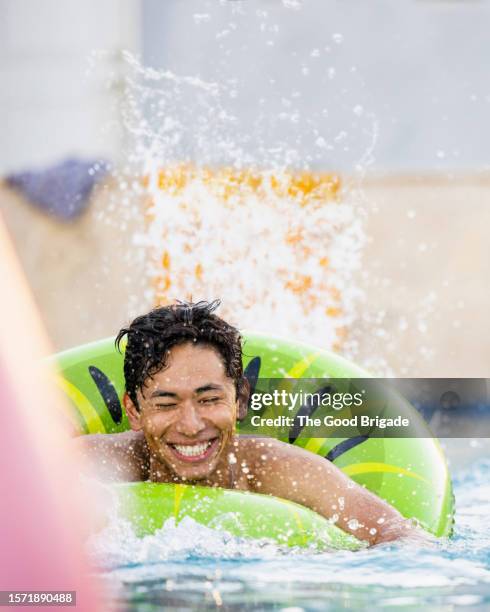 young man floating on pool raft and splashing water - man floating in pool stock pictures, royalty-free photos & images